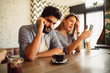 © Nebojsa - Young man with a beard is having phone call while he sitting with his girlfriend at cafe. She is checking balance on bank account via her phone.