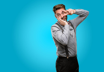 Canvas Print - Middle age man, with beard and bow tie looking at camera through fingers in victory gesture winking the eye and blowing a kiss