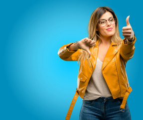 Wall Mural - Beautiful young woman confused with thumbs up and down, trying to take a decision expressing doubt and frustration, blue background