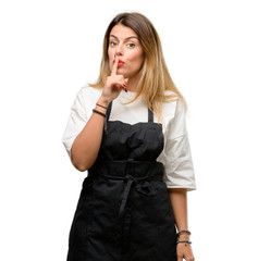 Poster - Shop owner woman wearing apron with index finger on lips, ask to be quiet. Silence and secret concept