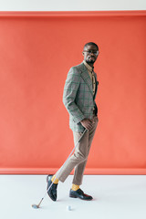 Wall Mural - handsome stylish african american man playing golf, on red