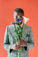 Wall Mural - fashionable african american man holding bouquet of flowers, isolated on red