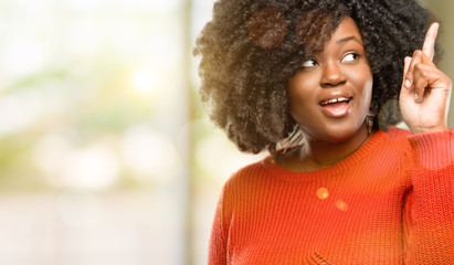 Poster - Beautiful african woman happy and surprised cheering expressing wow gesture pointing up, outdoor