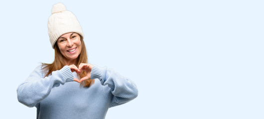 Middle age woman wearing wool winter cap happy showing love with hands in heart shape expressing healthy and marriage symbol isolated blue background