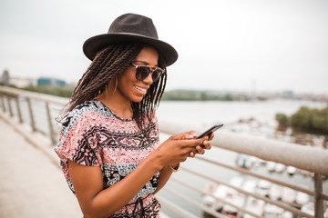 Young african american woman with black hat is on a river bridge