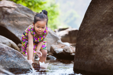 Wall Mural - Cute asian little child girl playing paper boat in the riverside in summer time with fun and happiness