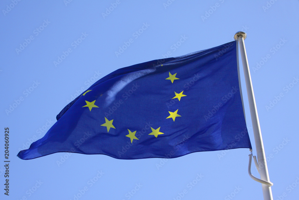 European Union EU flag on a pole waving in the wind with a blue sky on ...