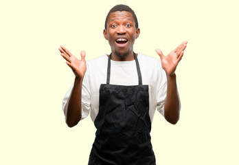 Poster - African man shop owner wearing apron happy and surprised cheering expressing wow gesture