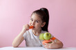© kaganskaya115 - A cute little girl eating fresh vegetables. A portrait on а pastel background. Healthy teeth.