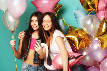 Two girls in stylish summer outfit , paper glasses and air balloons