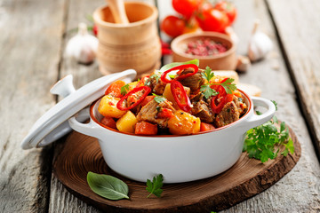 Wall Mural - Traditional goulash stewed meat with potatoes, carrots and vegetables on a  wooden background. 