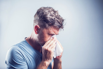 man sneezing in a tissue outdoors. pollen allergy, springtime.