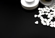 Details of small white pills spilling out of medicine container, isolated on black background