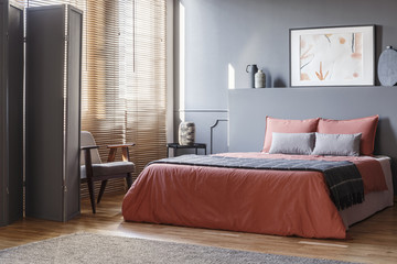 Real photo of elegant bedroom interior with black walls, brown blinds and orange sheets on gray bed