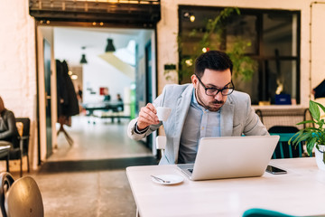 Wall Mural - Shocked man in eyeglasses reading news on laptop while drinking coffee. Making a face.