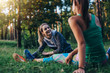 © undrey - Two cheerful female athletes warming up before training doing stretching exercise for legs sitting on grass