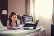 Businesswoman sitting on bed, using laptop. Young modern  woman executive on business trip working in  hotel room.