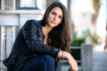 Gorgeous brunette beauty with long hair looking sexy in edgy leather jacket outdoors in urban setting