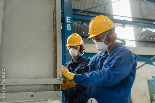 Cuadros en Lienzo Two blue-collar workers wearing protective equipment while insulating an industr