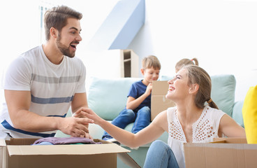 Poster - Young couple packing boxes with their children indoors. Happy family on moving day