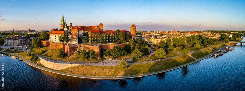Obraz Krakow, Poland. Wide aerial panorama at sunset with Royal Wawel castle and cathedral. Far view of  old city and old Jewish Kazimierz district. Vistula river bank, park, promenade and walking people fototapeta, plakat