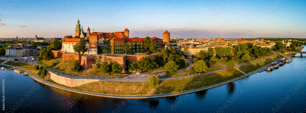 Krakow, Poland. Wide aerial panorama at sunset with Royal Wawel castle and cathedral. Far view of  old city and old Jewish Kazimierz district. Vistula river bank, park, promenade and walking people - obrazy, fototapety, plakaty 