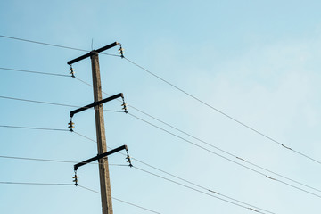 Posts with wires of high voltage on background of blue sky in sunlight. Background image of many wires in sky with copy space. Group of power lines.