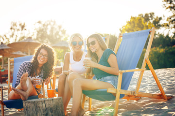 Wall Mural - Group of young casual female friends sitting on beach on sun beds,hangout and relaxing.