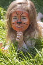 Portrait Of A Little Girl With Tiger Aqua Makeup, Lying On The Green Grass