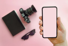 Hand Showing Stylish Black Phone With Empty Screen, Sunglasses,camera And Notebook On Pink Background, Flat Lay. Modern Hipster Image. Instagram Blogging. Summer Vacation