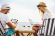 © Mediteraneo - Happy smiling couple surfing the net and enjoy the summer at tropical beach using laptop and digital tablet