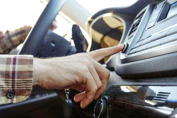 Young man in checkered hipster shirt pressing buttons on car multimedia panel, switching shifting radio station knob. Close up of male hand on vehicle dashboard setting fm radio. Background, side view
