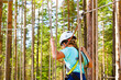 © Александр Чернышов - Teenage girl goes on hinged trail in extreme rope Park in summer forest. High-altitude climbing training of child on adventure track, equipped with safety straps and protective helmet. Estonian summer