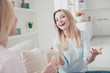 © deagreez - Portrait of laughing cheerful positive girl joking sharing secrets with her mother having mugs with tea cacao beverage in hands cozy comfort atmosphere enjoying meeting indoor sitting on sofa