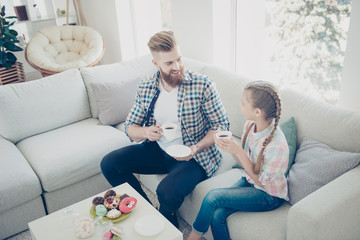 Poster - Portrait of stylish bearded trendy dad with red hair drinking beverage with little cute kid with hairstyle having sweets on the table holding mugs and saucers looking at each other enjoying talk