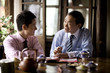 © Erickson Stock - Mature adult businessman sitting with a young adult male colleague drinking tea at a cafe.
