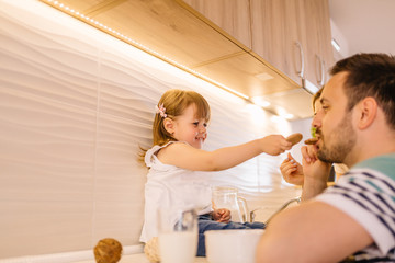 Wall Mural - Young daughter is feeding her father with cookies