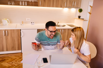 Wall Mural - Smiling satisfied couple buying online with credit card at home