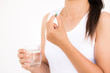 © Siam - medicine, health care and people concept - close up of woman taking in pill and another hand holding a glass of clean mineral water.