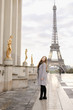 European woman in grey coat standing on Trocadero square near gilded statues and Eiffel Tower in Paris. Concept of trip to France and European landmarks.