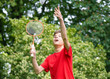 Young teen boy playing badminton in meadow with forest in background. Child with badminton rackets in hand. Kid have fun in summer park at day.