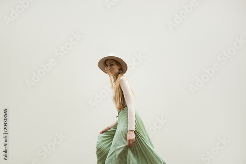 Cuadros en Lienzo Young red hair girl in hat, dressed in beige blouse and turqoise pleats skirt, on light street backgraund