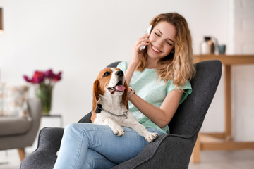 Wall Mural - Young woman talking on phone while stroking her dog at home