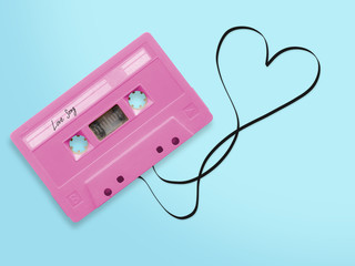 pink audio cassette tape with label tag love song tangled tape ribbon heart shape isolated on blue background, top view.