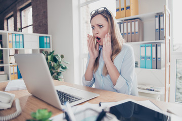 Portrait of attractive, excited, shocked, stressed woman with wide open mouth holding palms near face, looking at screen of computer, sitting in work place, station at desktop