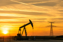 Pumpjack And Transmission Towers At Sunset Symbolizing Energy Transition. A Pump Jack Pumping Oil Out Of A Well With Silhouettes Of Electricity Pylons And Power Line Against A Red Sky.