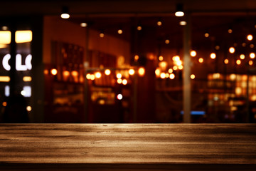 Wall Mural - Image of wooden table in front of abstract blurred restaurant lights background.