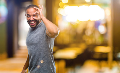 Poster - African american man with beard looking at camera through fingers in ok gesture. Imitating binoculars, beautiful eyes and smile at night