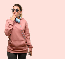 Wall Mural - Young sport woman with headphones and sunglasses looking at camera showing tong and making victory sign with fingers