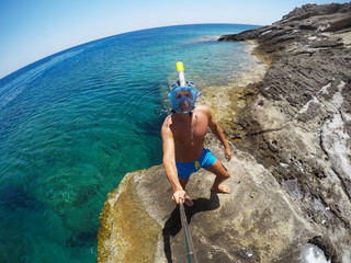 Wall Mural - Underwater view of a young diver man swimming in the turquoise sea under the surface with snorkeling mask for summer vacation while taking a selfie with a stick.